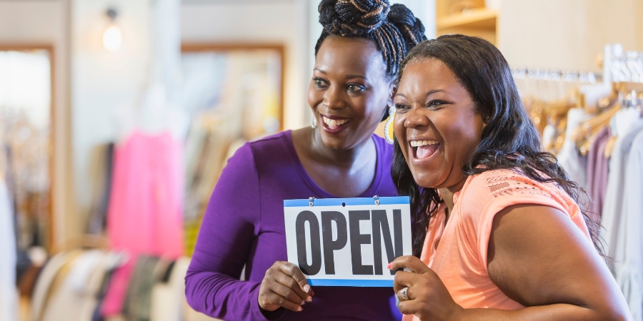 Two Black women holding an "Open" sign
