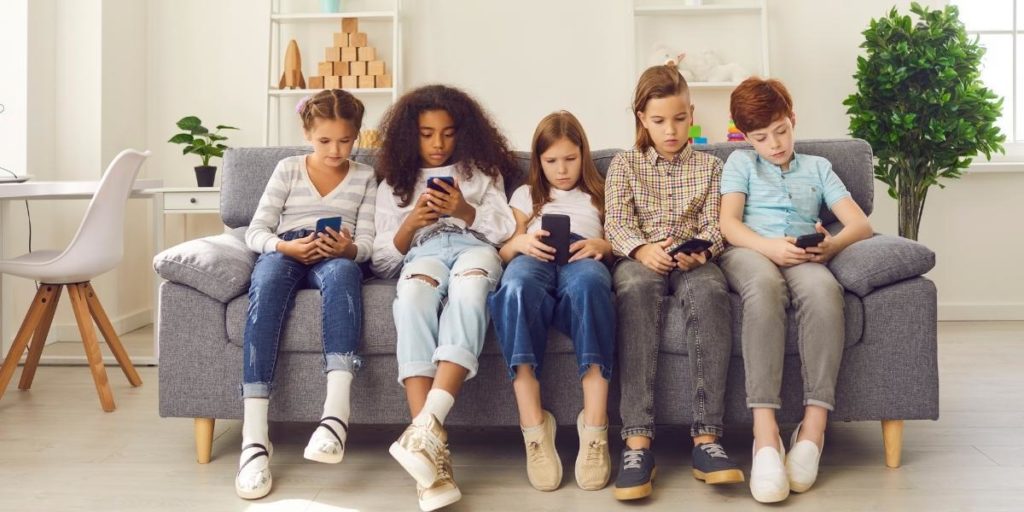 Group of young kids sitting on a couch holding cell phones