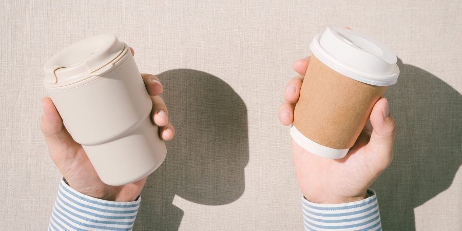 Close-up of someone holding a reusable cup in one hand and a paper cup in the other